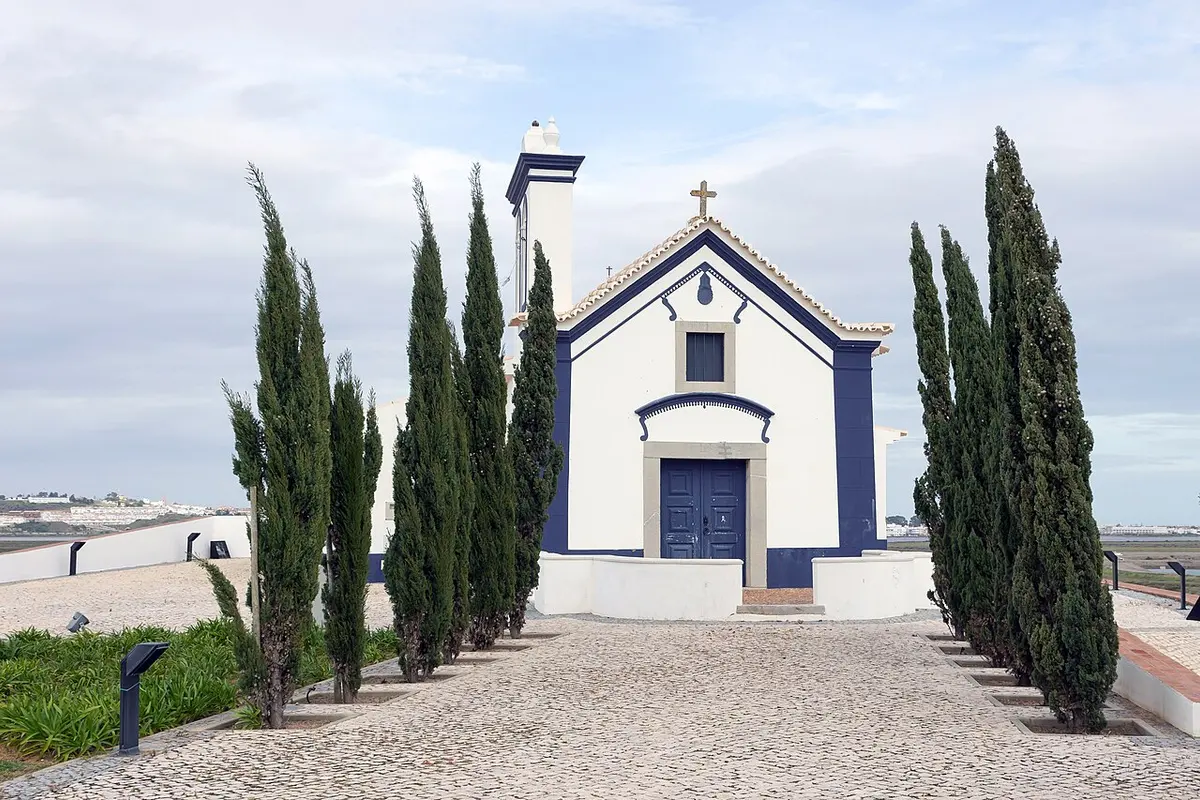 Blue-edged white chapel between tall cypress trees in Castro Marim