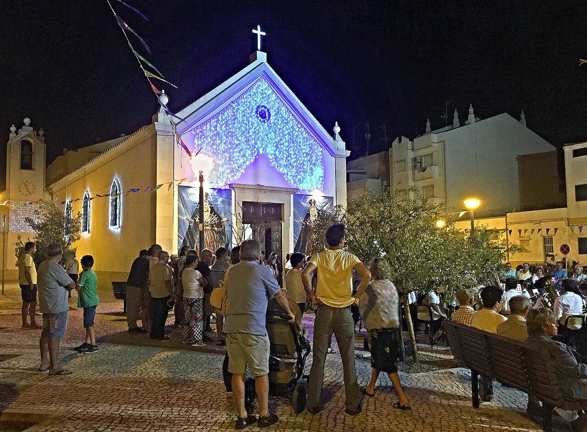 People gathered outside the illuminated parish church during a religious celebration in Monte Gordo