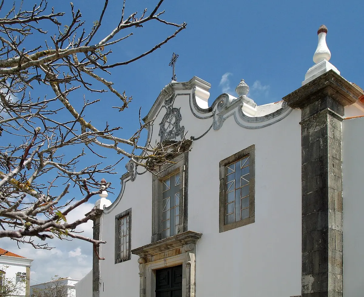 White parish church façade behind trees in São Brás de Alportel