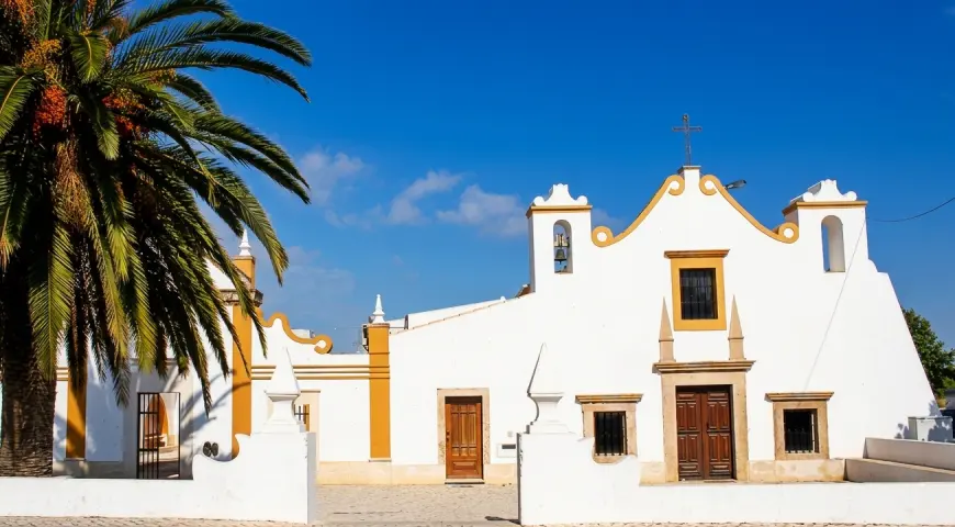 The white Nossa Senhora da Guia chapel with yellow detailing and palm trees
