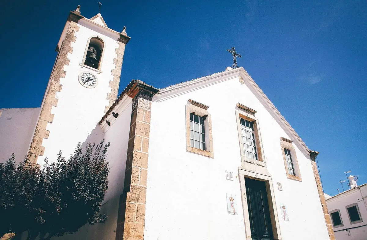 The facade and clock tower of Paderne parish church viewed from below