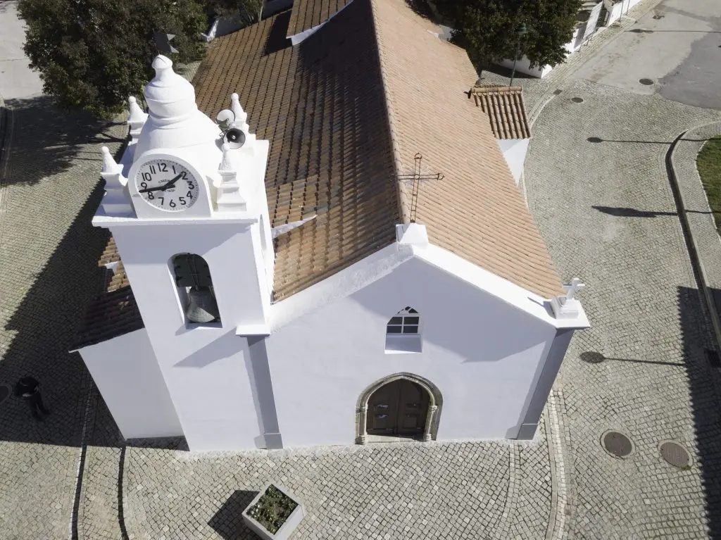 An elevated view of São Romão church’s white façade and bell tower in Alferce