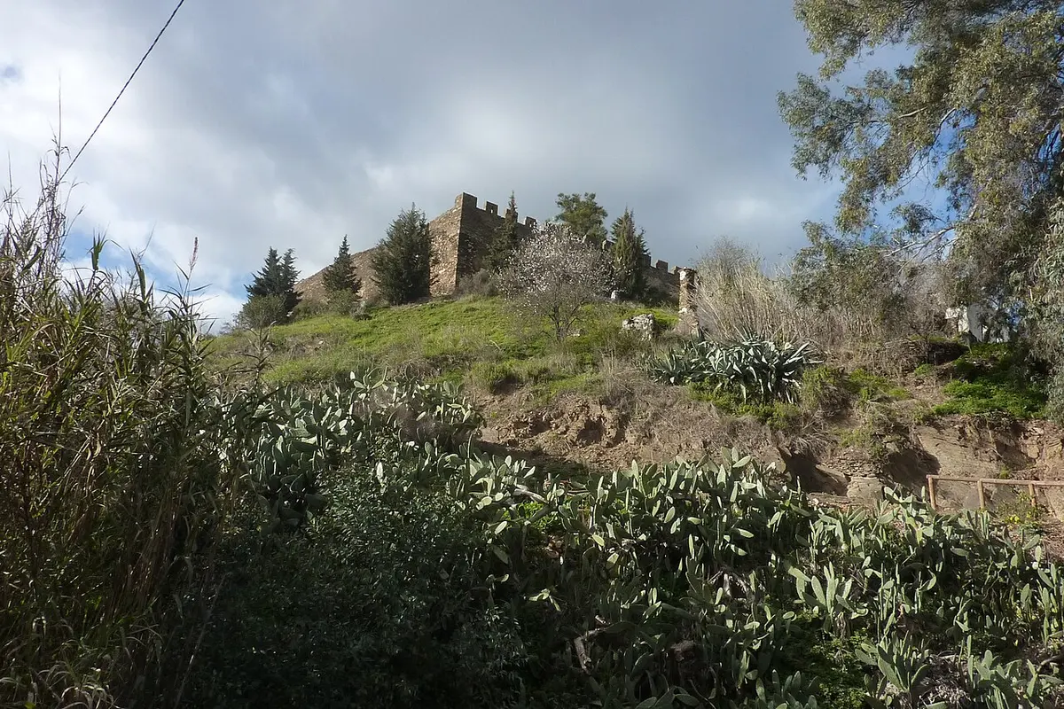 Crenellated walls of Alcoutim Castle above a slope of prickly pear cactus and trees