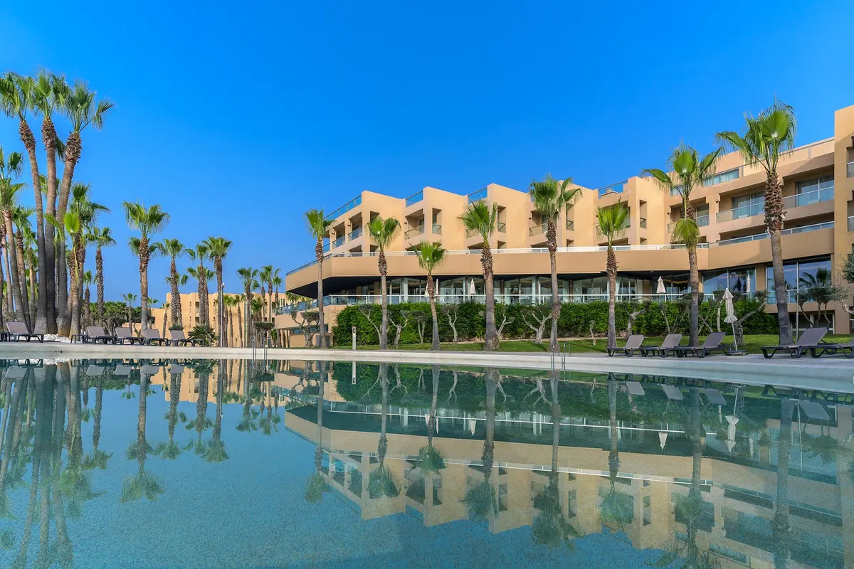 Palm trees and the hotel building reflected in a pool at NAU São Rafael Suites