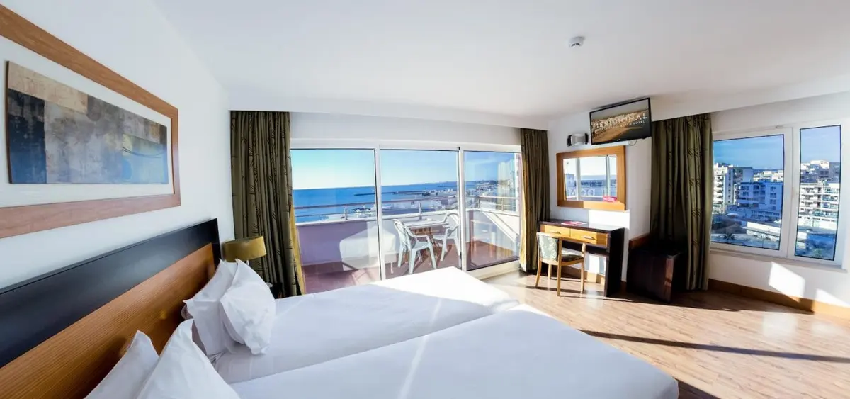 A bright guest room at Hotel Quarteirasol with twin beds and a balcony looking towards the sea