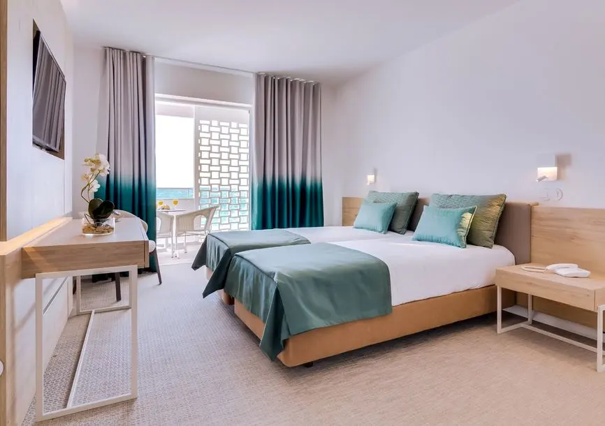 A hotel bedroom at Sol e Mar with turquoise textiles and a balcony doorway