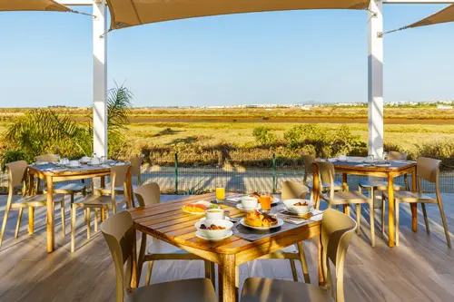 Tables on a shaded dining terrace overlooking the lagoon at AP Cabanas