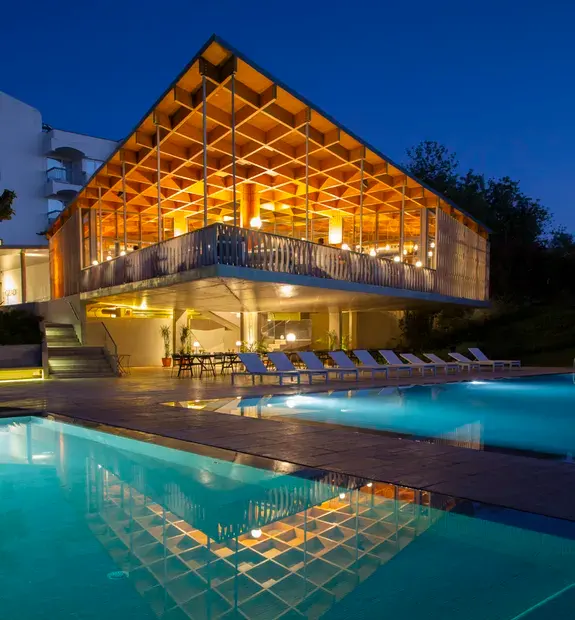 Pool and warmly lit timber roof at OZADI Tavira Hotel at night