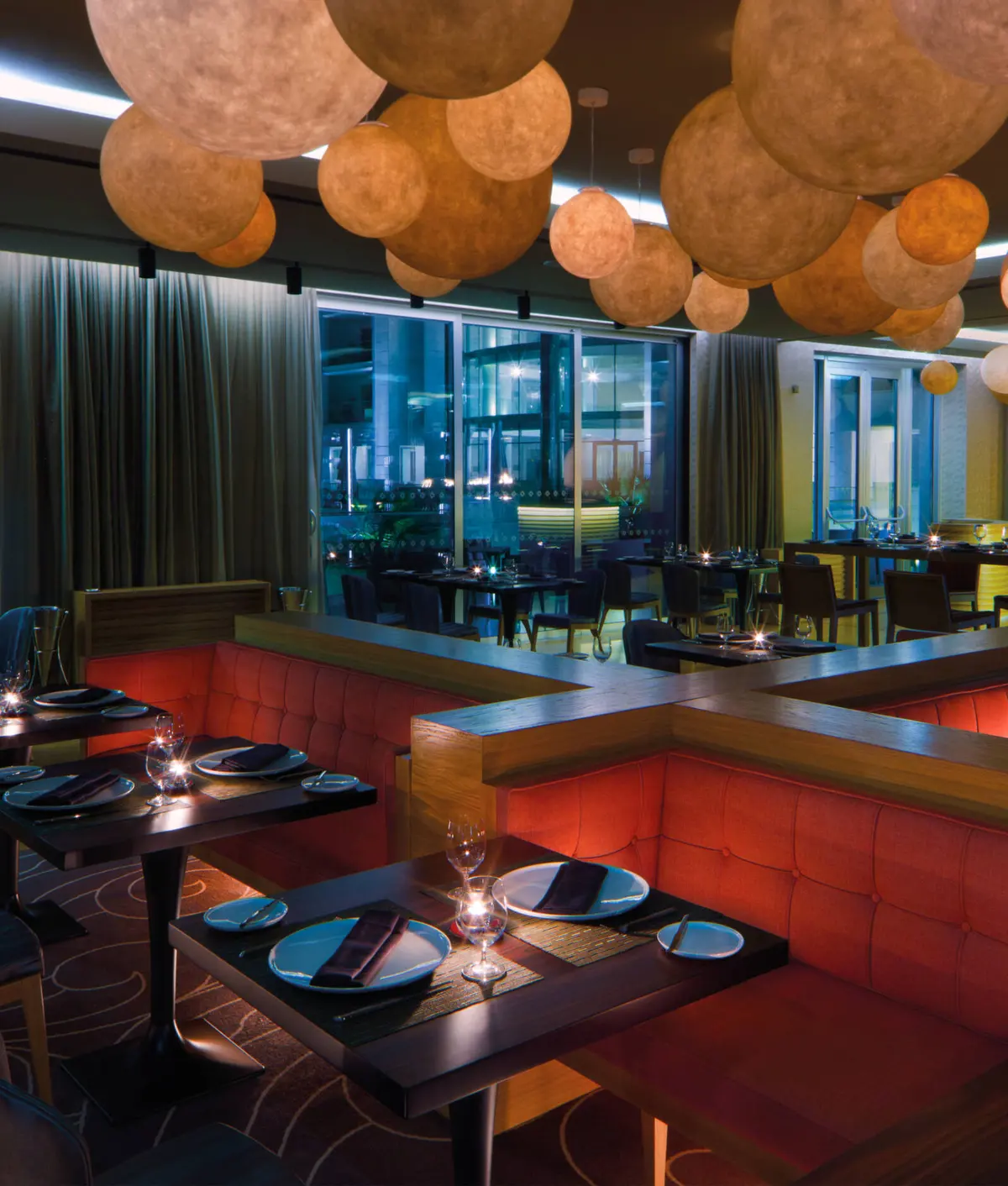 Warm pendant lights above red banquettes and set dining tables inside Gusto at Conrad Algarve