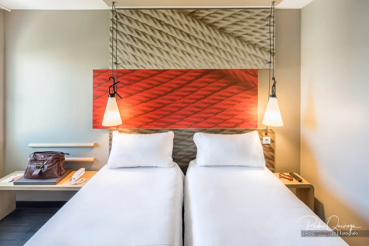 Twin beds and pendant lights against red and sand-textured headboards in a guest room at ibis Faro Algarve