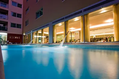 The blue pool beside the illuminated windows of Monte Gordo Hotel, Apartamentos & Spa at dusk
