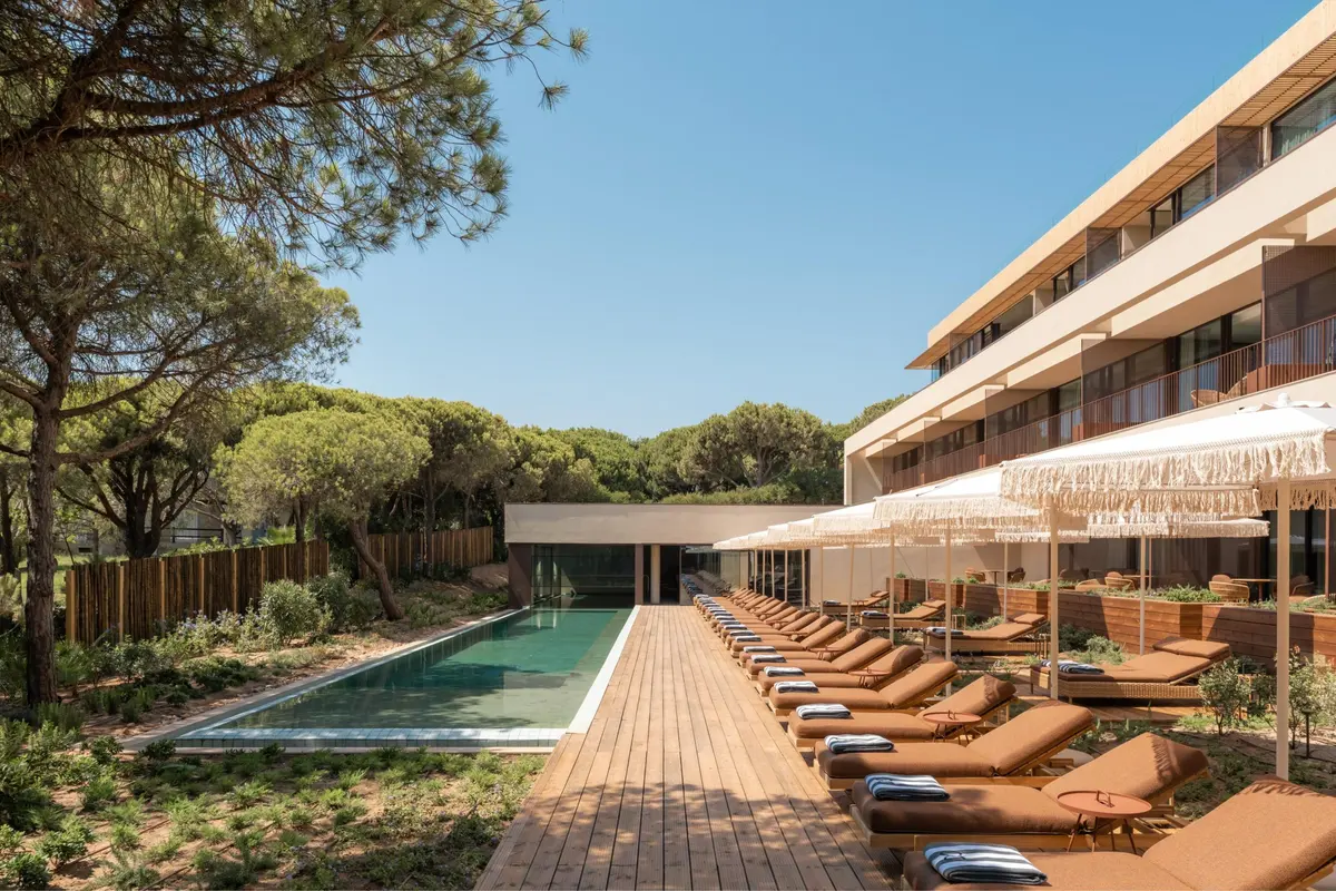 A long outdoor swimming pool beside pine trees, terracotta loungers and the Praia Collection building at Octant Praia Verde