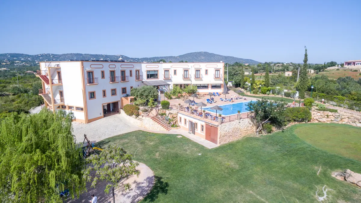 An elevated view of the pale hotel buildings, blue swimming pool and green grounds at Quinta dos Poetas