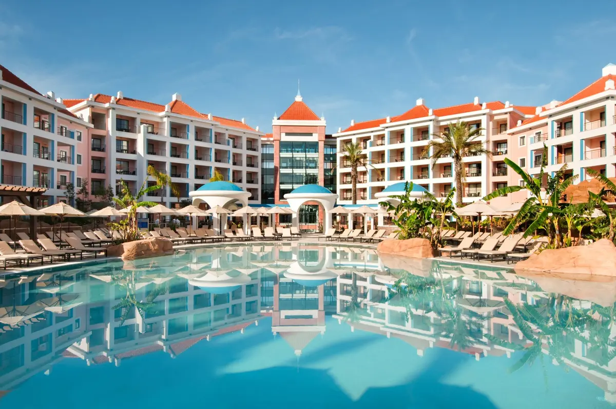 A turquoise pool reflecting the pink hotel buildings and red tiled roofs at Hilton Vilamoura