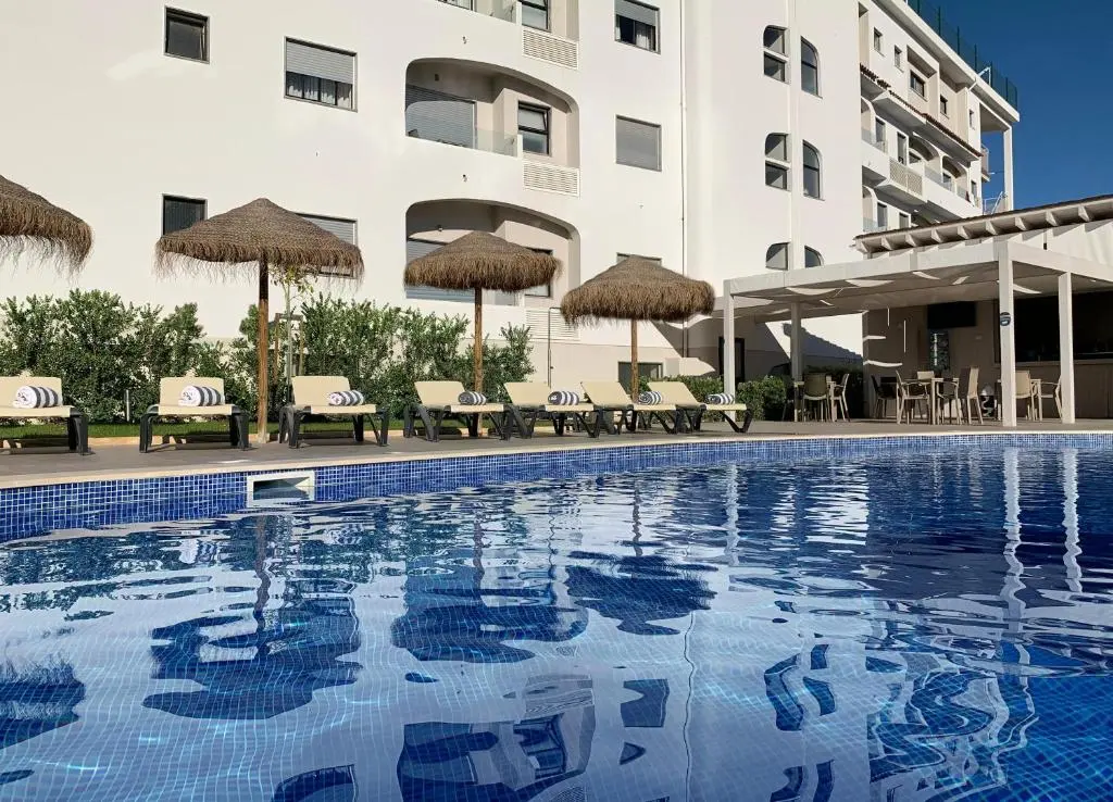 The blue pool, parasols and curved balconies of Água Hotels Alvor Jardim