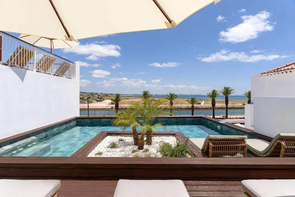 A small pool and sun loungers between white hotel terraces, with the Lagos waterfront beyond