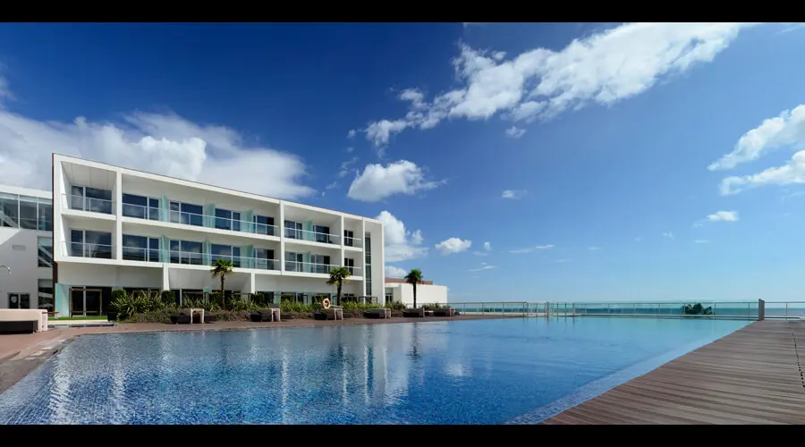 A white terraced hotel building and infinity pool facing the sea, now Iberostar Selection Lagos Algarve