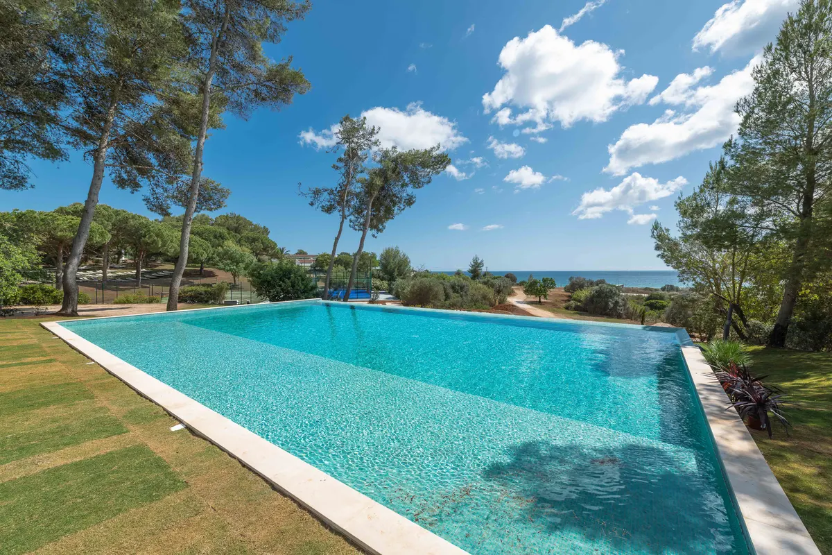 A blue infinity pool surrounded by lawn and pine trees at the former Pestana Delfim, now Pestana Blue Alvor Beach