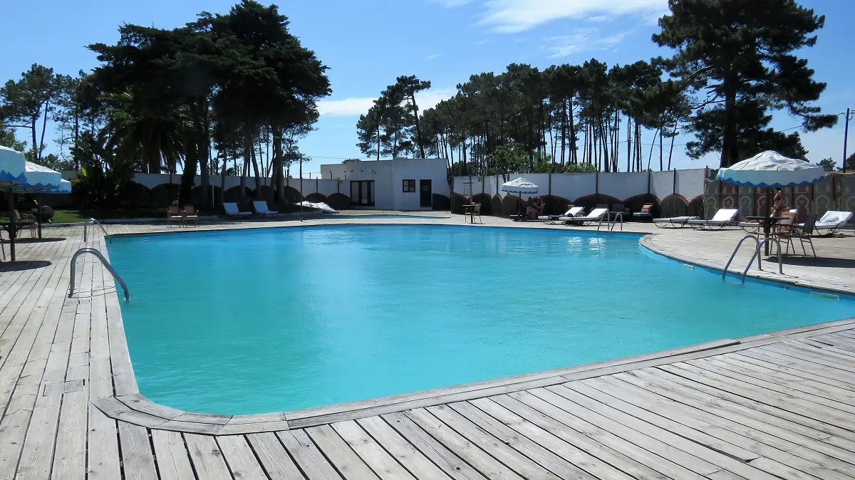 The blue outdoor swimming pool, wooden deck and pine trees at Hotel Vale da Telha