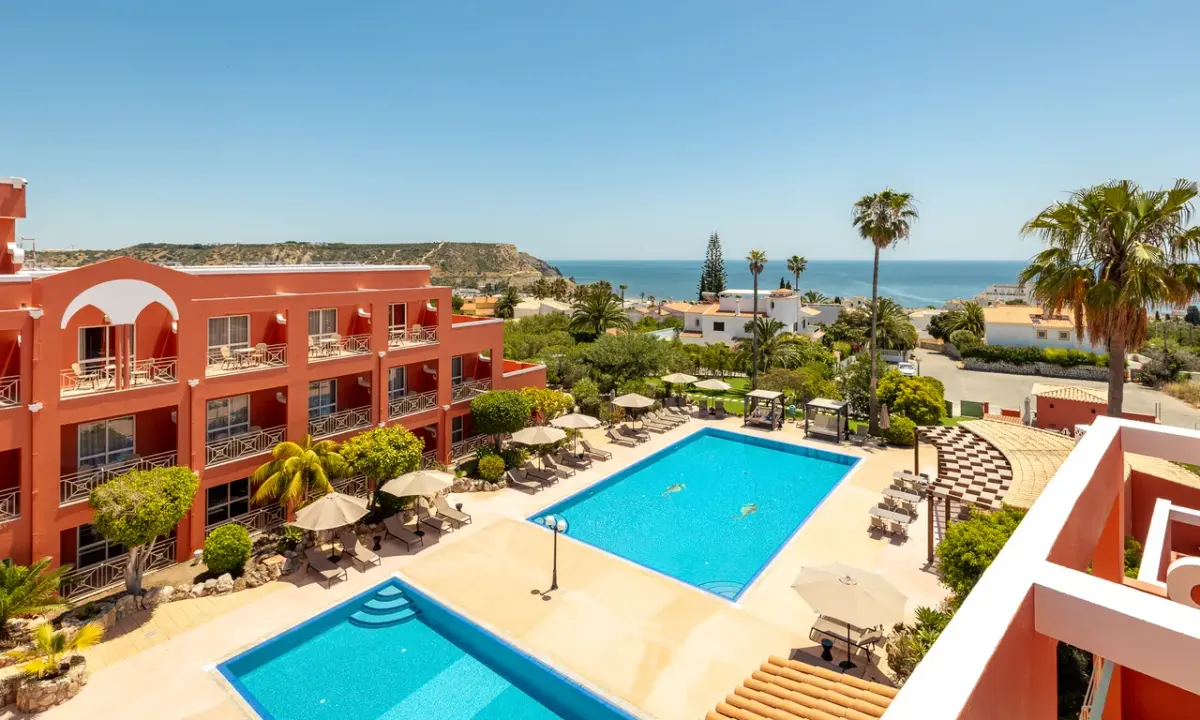 The red hotel buildings and swimming pools at Belavista da Luz Wellness & Lifestyle Hotel, with the coast beyond