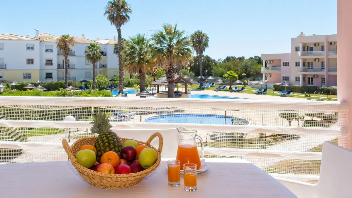 A poolside table and the accommodation buildings around the pool at TURIM Estrela do Vau