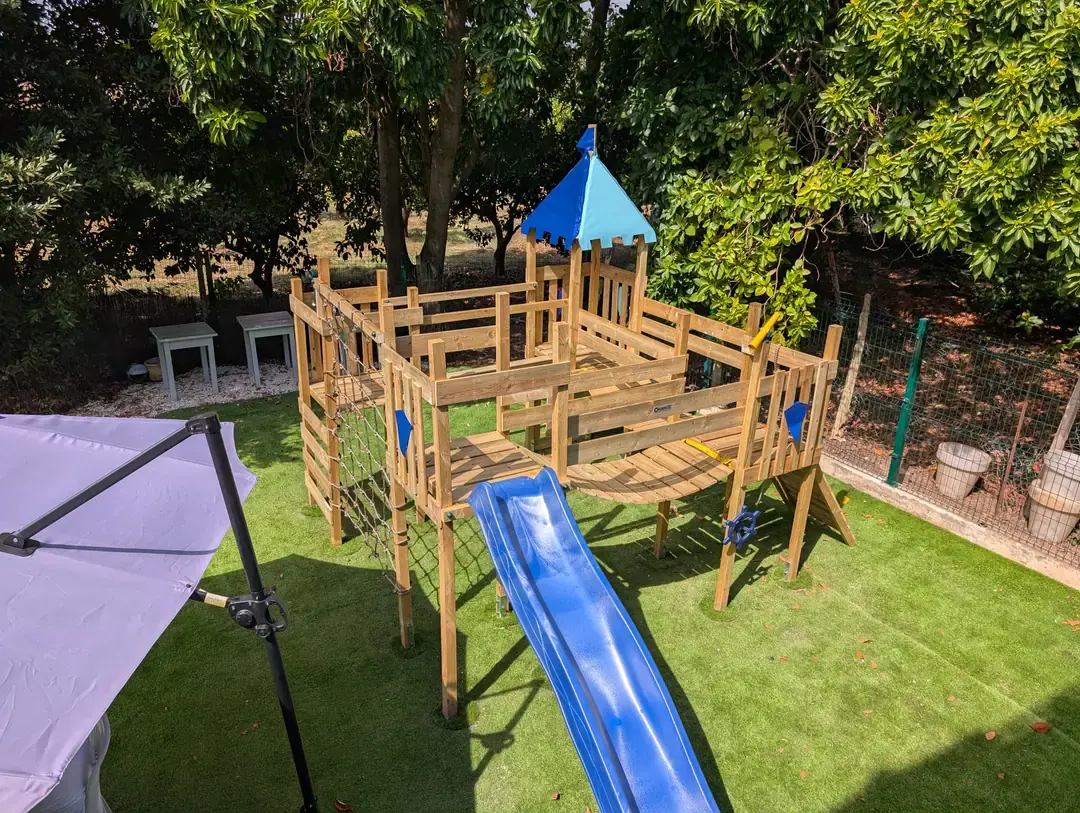 Wooden play castle and blue slide in Zazoo's outdoor play area in Almancil