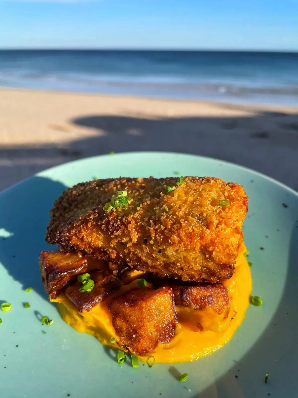 A salmon dish on a blue plate with Praia da Luz behind it