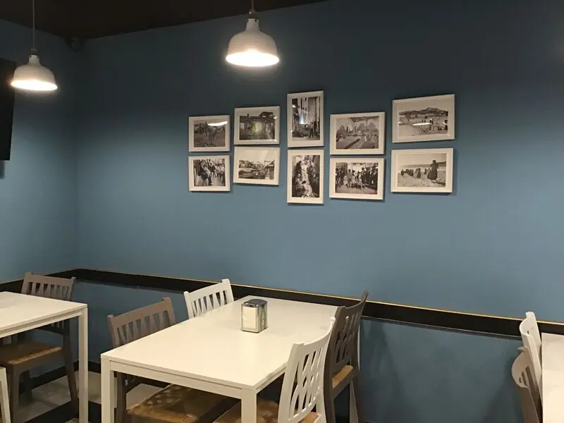 White tables and chairs against a blue wall displaying historical photographs at Café da Vila in São Brás.