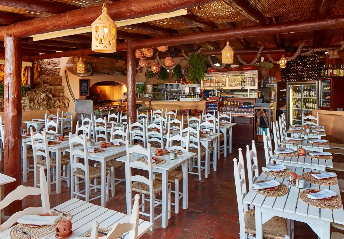 White wooden tables and chairs beneath the decorated wooden ceiling at Caniço