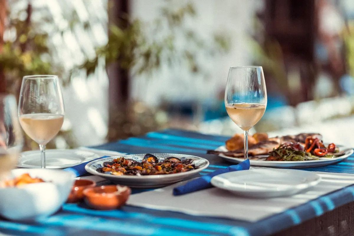 Food and glasses of wine on a blue table at Cato in Carrapateira