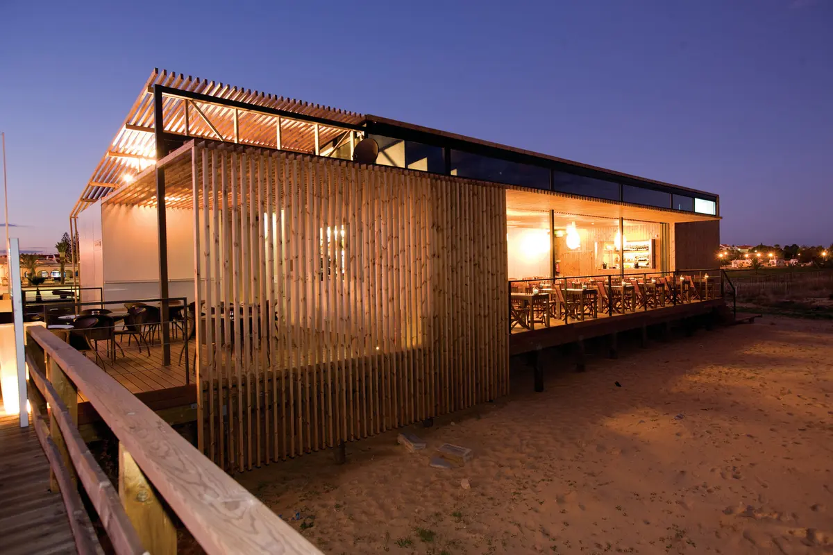 The timber-sided Chá com Água Salgada restaurant and terrace beside Manta Rota beach at dusk.