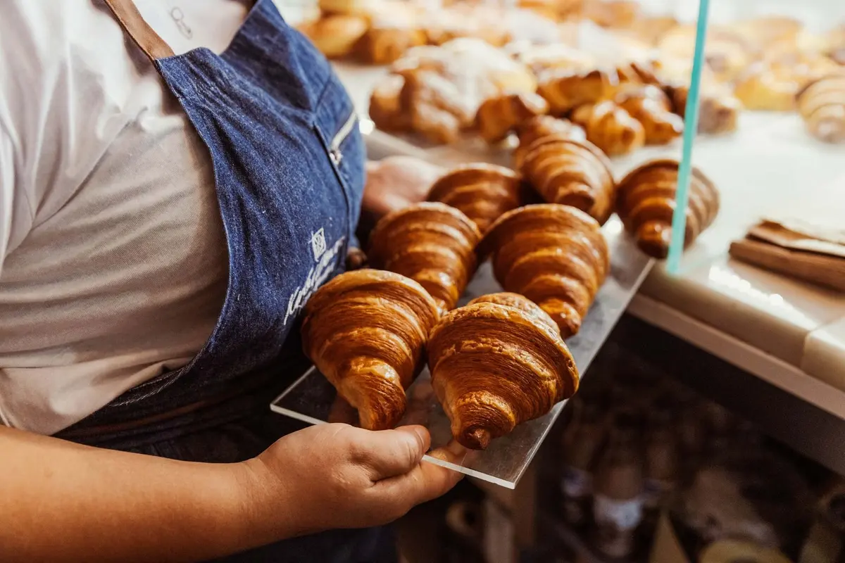 A tray of croissants held at the pastry counter by a person wearing a Kubidoce apron.