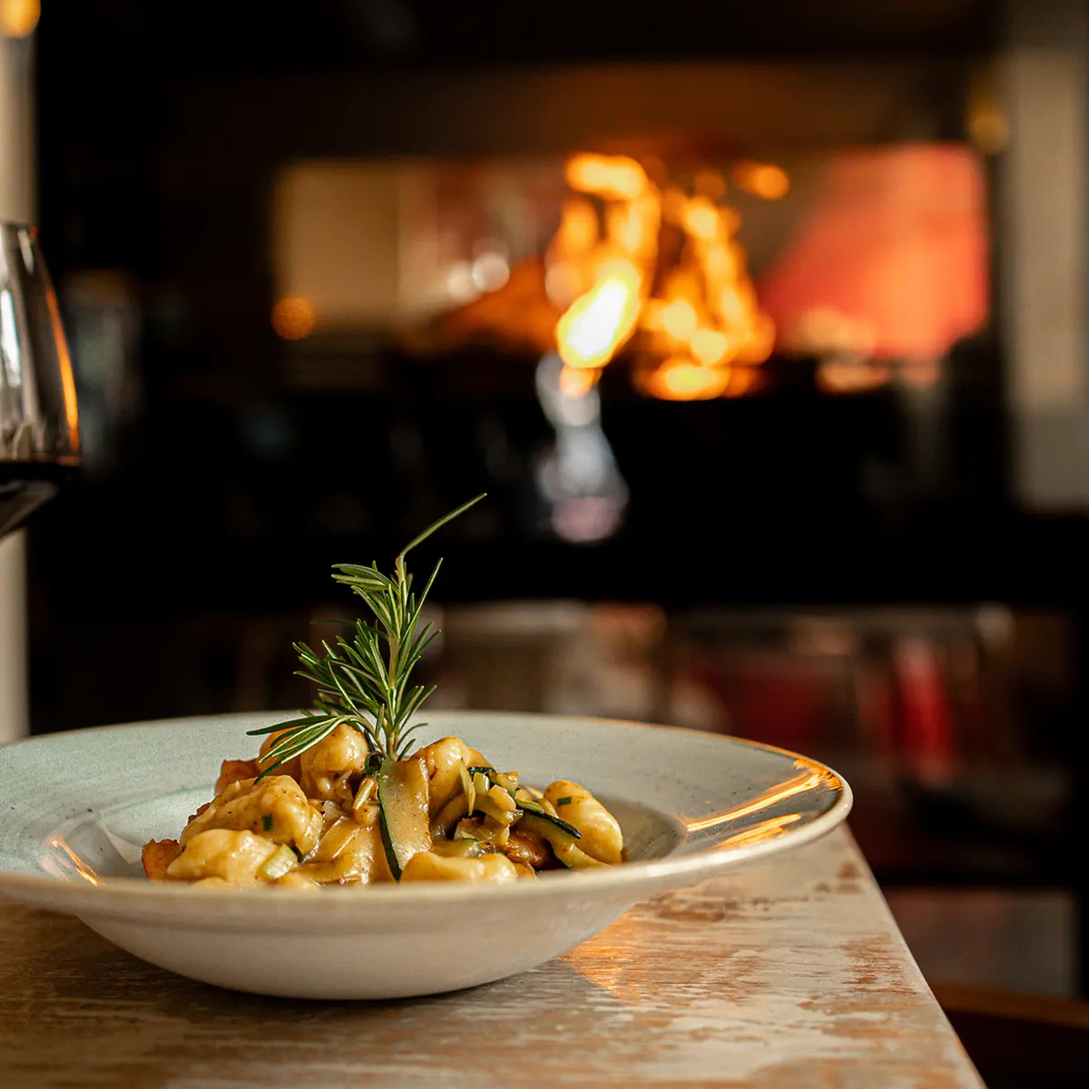 A bowl of pasta in the foreground with a softly lit restaurant kitchen behind it at l’Osteria Faro.