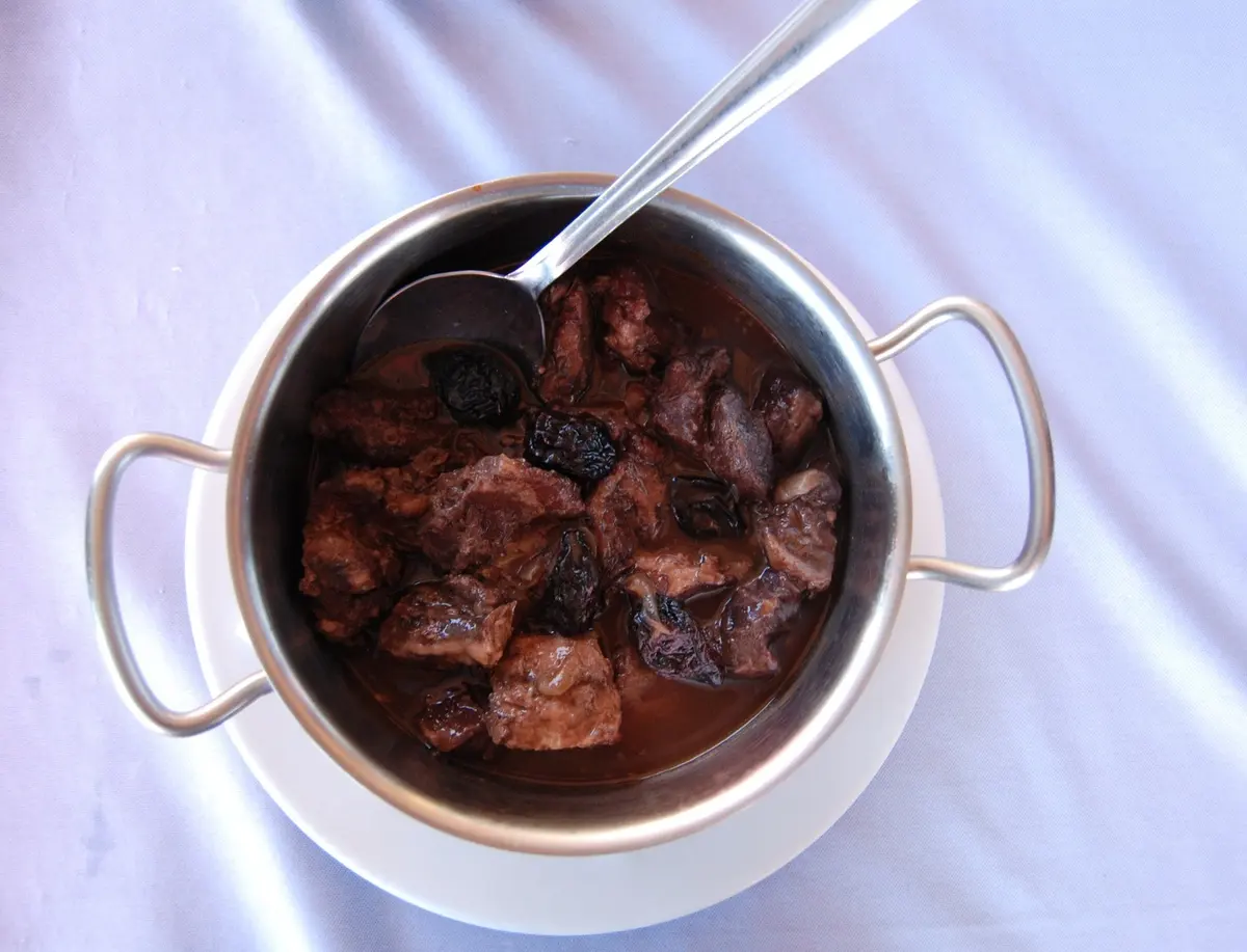 A small pan of wild boar stew presented on a white tablecloth