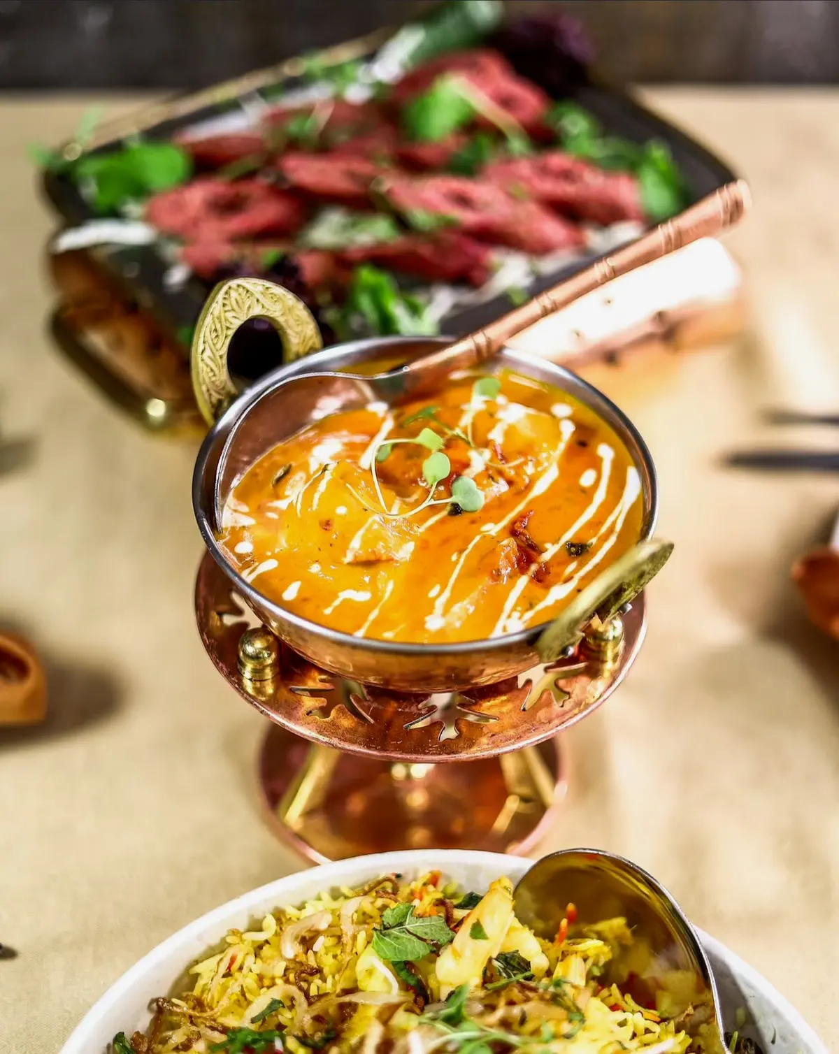 A curry served in a metal bowl with rice and grilled dishes behind it, from Namastey’s official gallery.