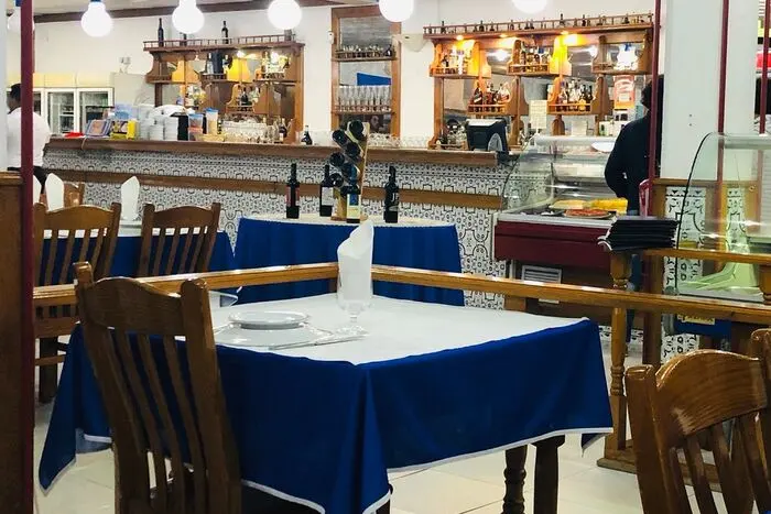 Tables with blue and white tablecloths inside O Franguinho, with the service counter behind.