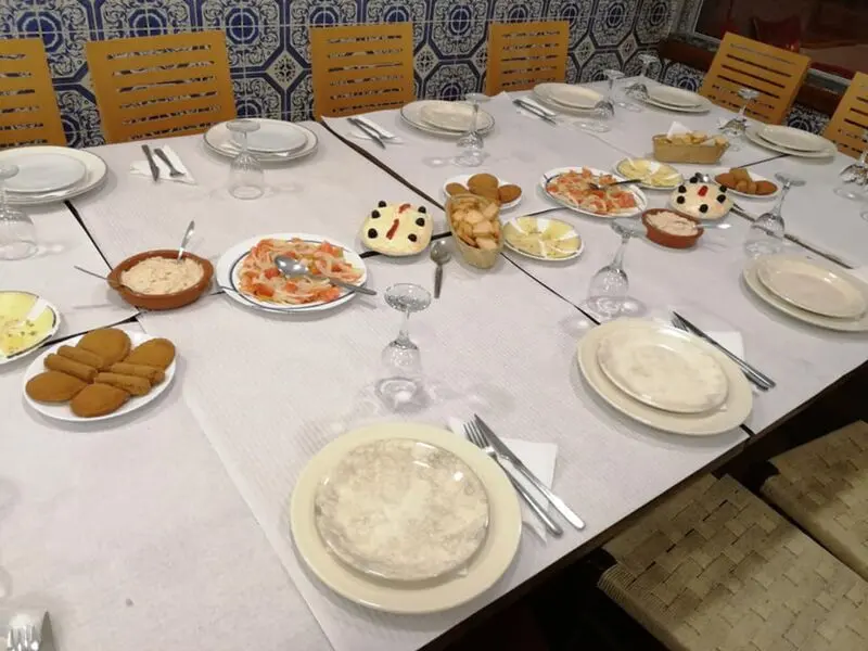 A table laid with small dishes, cheese and bread against blue-and-white tiles at Tapas e Petiscos O Paixão.