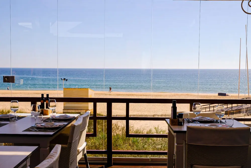 Restaurant tables at Pézinhos n’Areia looking through glass towards Praia Verde beach and the sea.