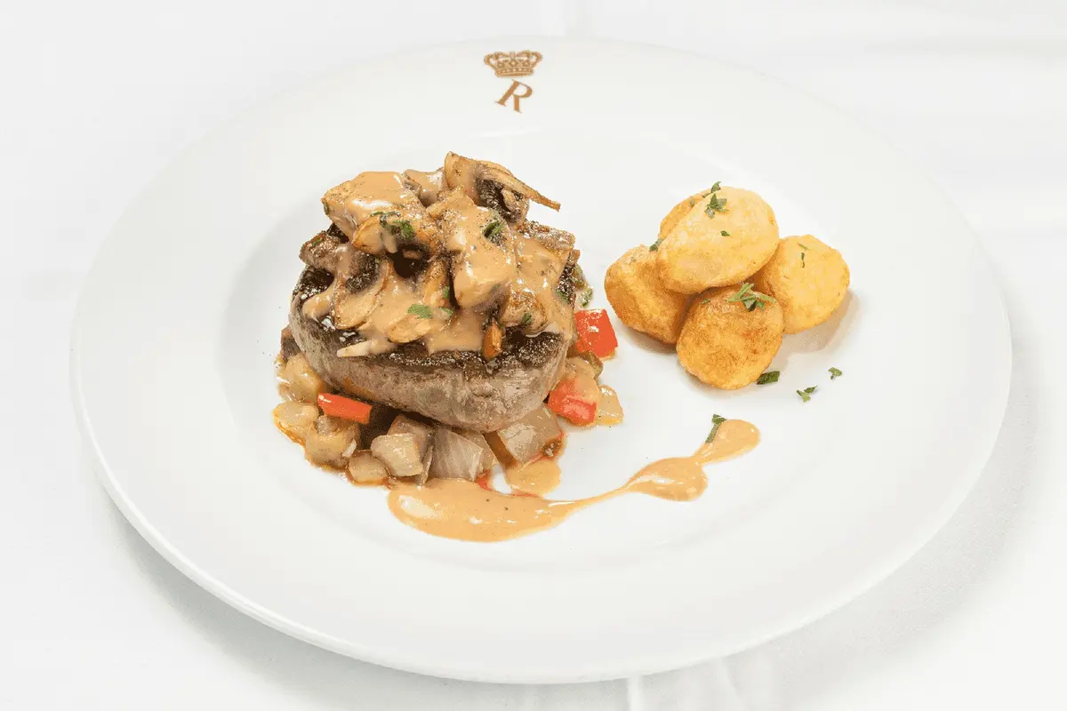 A plated meat dish with potatoes on a Rei das Praias restaurant plate