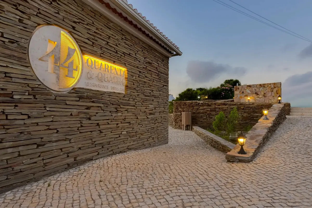 The illuminated Quarenta & Quatro restaurant sign beside a stone wall and paved entrance