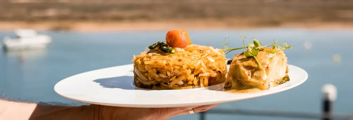 A plated dish held above the lagoon-facing terrace at Sabores da Ria in Cabanas.