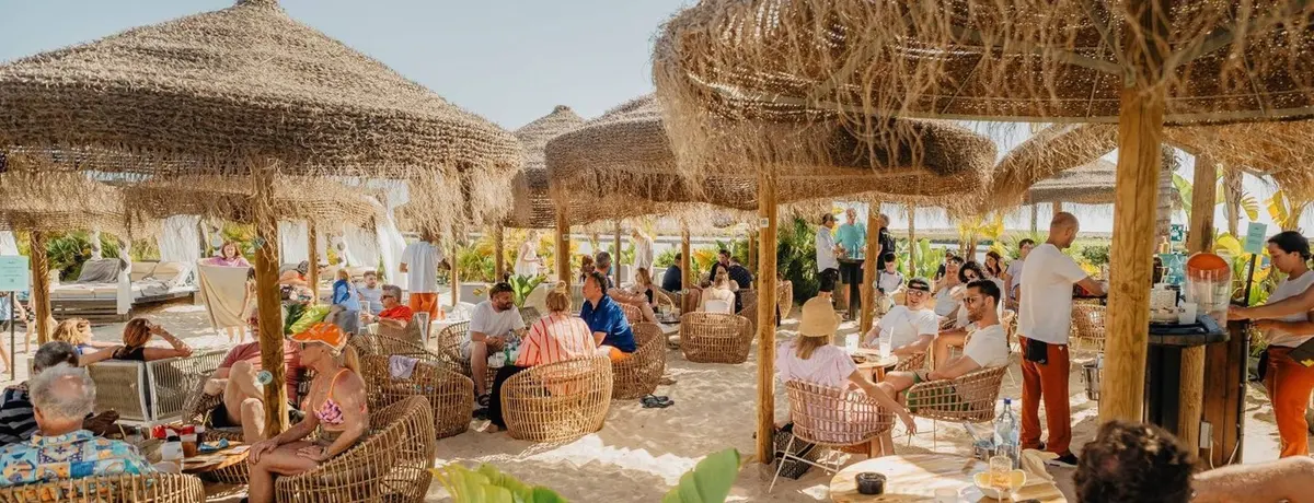 Visitors seated beneath thatched parasols at The Shack beside the Quinta do Lago lake