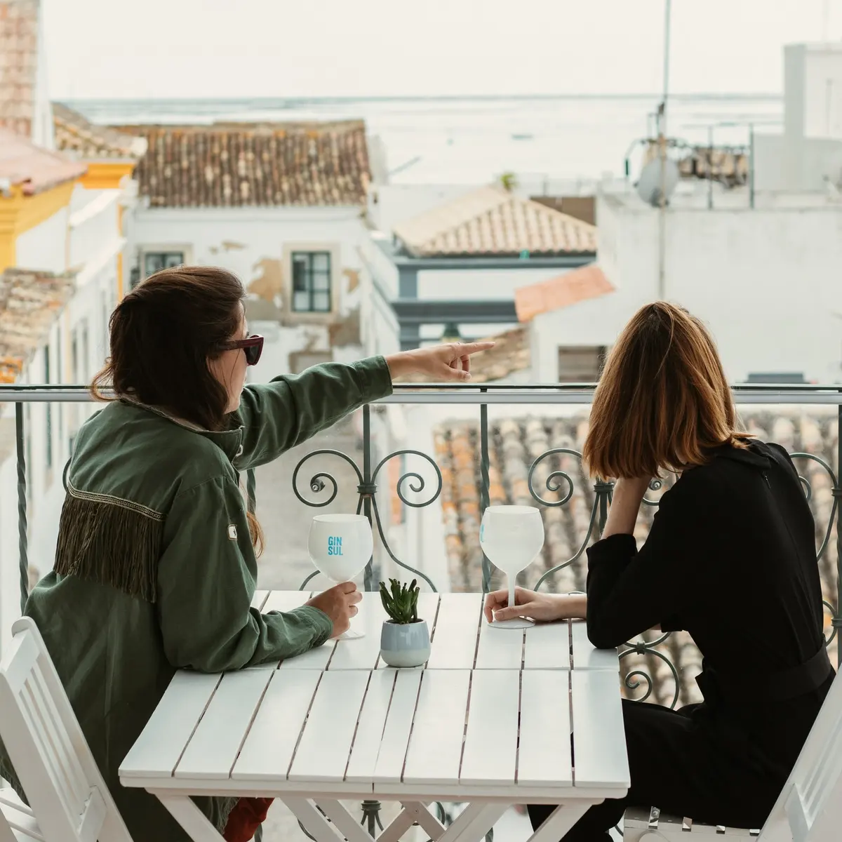 Two guests seated on Vila Adentro’s rooftop terrace with Faro’s old-town roofs and the lagoon beyond.