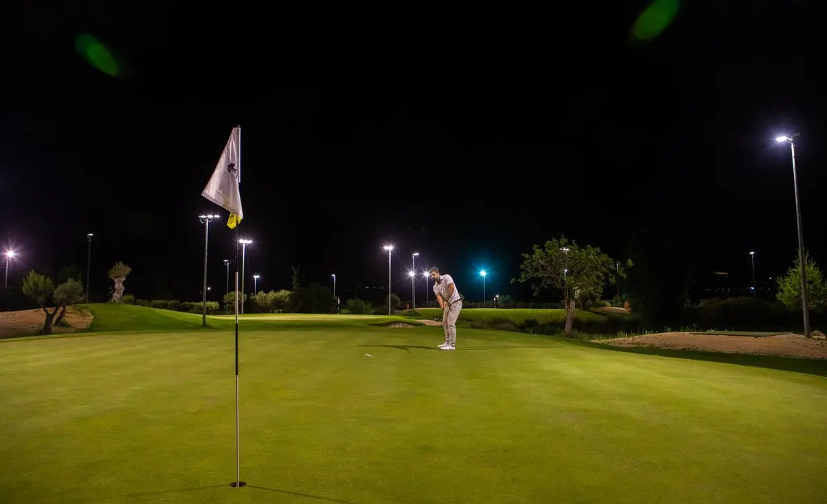 A golfer putting on Amendoeira’s floodlit Academy Course at night