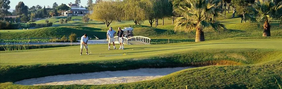 Golfers on a green beside a pond and palms at Pinheiros Altos
