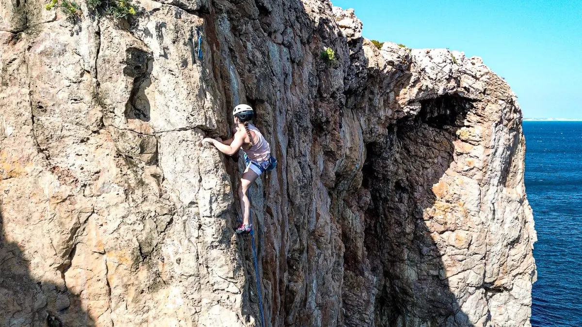 A helmeted climber on a coastal limestone face above the sea