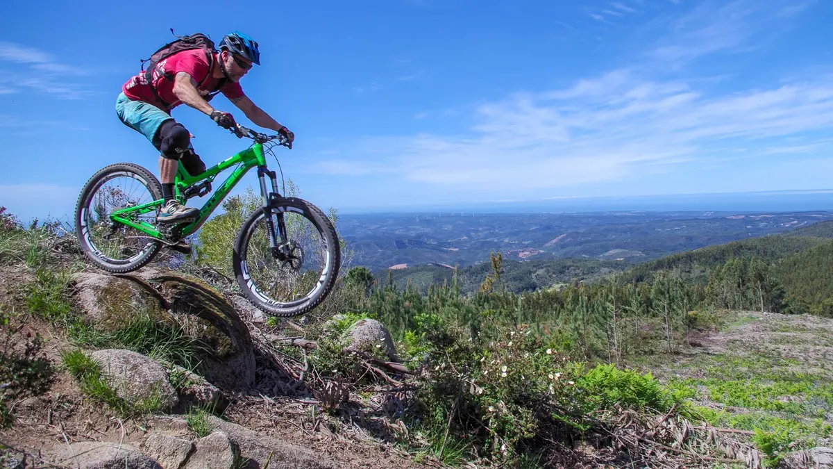 A mountain biker riding over a rocky rise with the Algarve hills behind