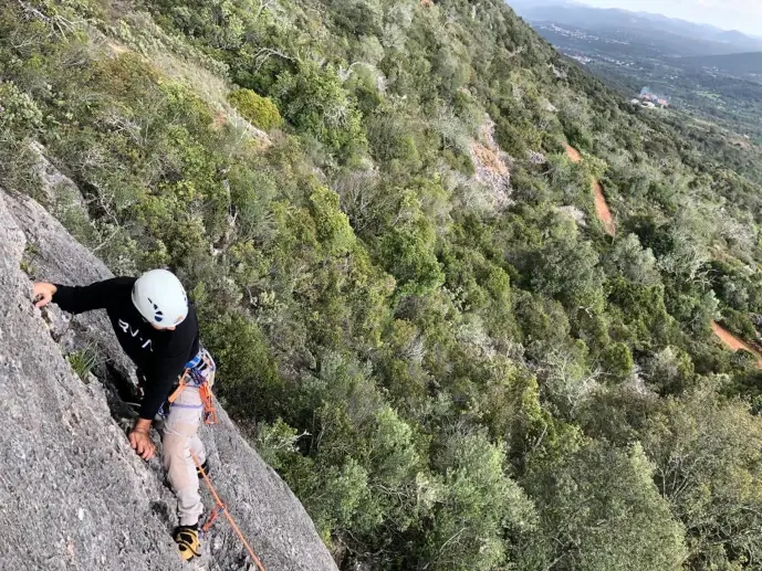 A roped climber on a slab above the wooded landscape at Rocha da Pena