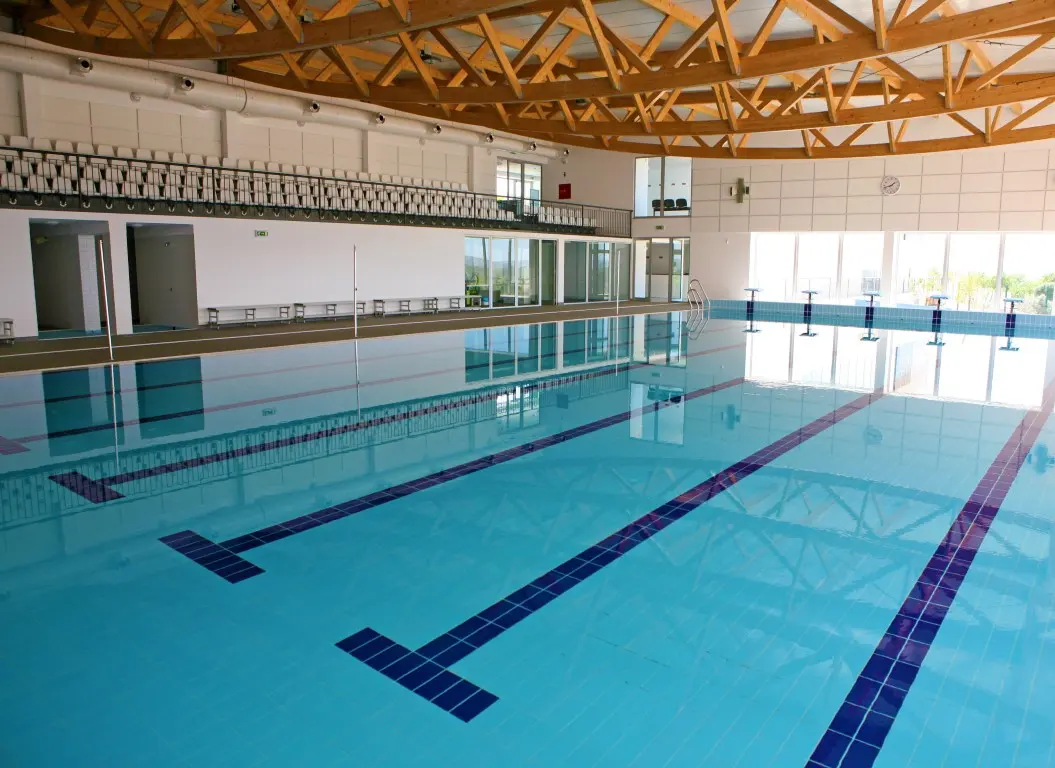 Empty swimming lanes beneath timber roof trusses at Mexilhoeira Grande Municipal Sports Complex