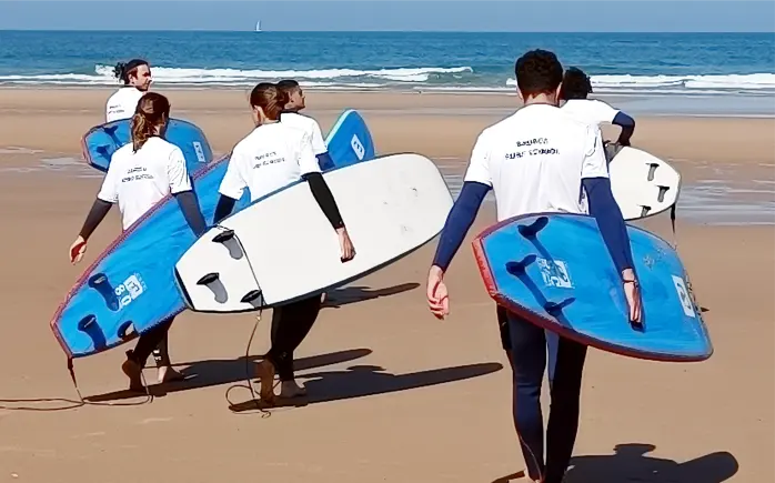 Students in Sagres Surf School shirts carrying boards towards the sea